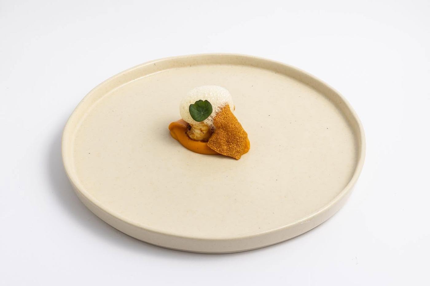 Entrante con crema anaranjada y hoja de hierba