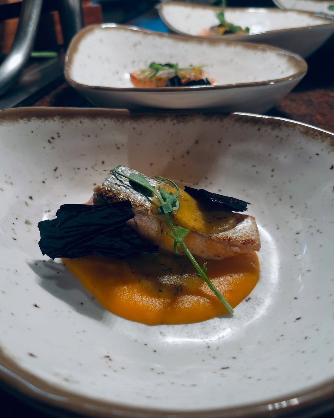 Pescado sobre crema de calabaza con crujientes negros